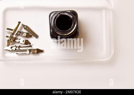 Tintenflasche mit Metallspitzen für Tintenstift auf weißem Hintergrund. Schreibwaren auf weißem Schreibtisch, Nahansicht von oben. Rechtschreibunterricht und Caligraphie-Übungen. T Stockfoto
