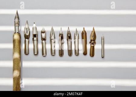 Metallspitzen für den Tintenstift auf weißem Hintergrund bei Sonneneinstrahlung. Schreibwaren auf weißem Schreibtisch, Nahansicht von oben. Rechtschreibunterricht und Caligraphie-Übungen. Stockfoto