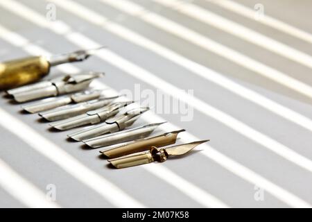 Metallspitzen für den Tintenstift auf weißem Hintergrund bei Sonneneinstrahlung. Schreibwaren auf weißem Schreibtisch, Nahansicht von oben. Rechtschreibunterricht und Caligraphie-Übungen. Stockfoto