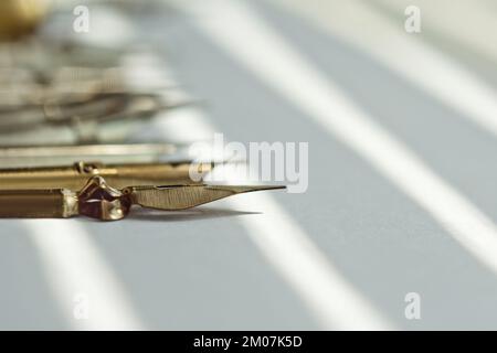 Metallspitzen für den Tintenstift auf weißem Hintergrund bei Sonneneinstrahlung. Schreibwaren auf weißem Schreibtisch, Nahansicht von oben. Rechtschreibunterricht und Caligraphie-Übungen. Stockfoto