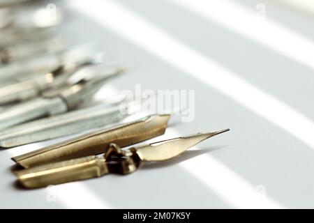 Metallspitzen für den Tintenstift auf weißem Hintergrund bei Sonneneinstrahlung. Schreibwaren auf weißem Schreibtisch, Nahansicht von oben. Rechtschreibunterricht und Caligraphie-Übungen. Stockfoto