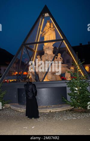 Ein Priester meditiert vor einem Brunnen mit der Jungfrau Maria. Stockfoto