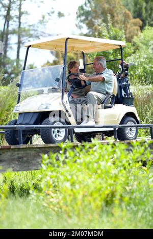 Im Ruhestand und in Lebensfreude. Ein reifes Paar, das sein letztes Loch bespricht, während es einen Golfwagen fährt. Stockfoto