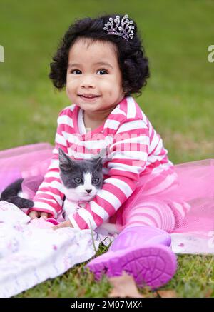 Mein kleiner, fauler Schwanz. Süßes kleines Mädchen, das draußen mit ihrem Kätzchen auf einer Decke sitzt. Stockfoto