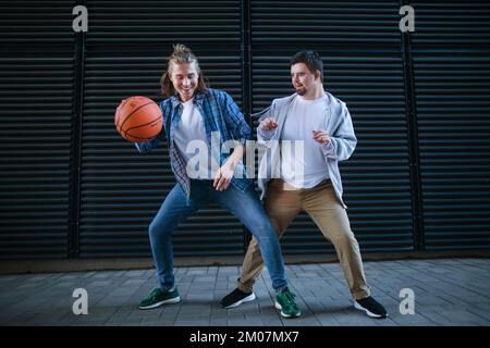 Ein Mann mit Down-Syndrom, der mit seinem Freund Basketball spielt. Freundschaftsbegriff und gesellschaftliche Integration Behinderter. Stockfoto