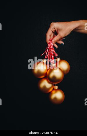 goldene weihnachtsbälle in Frauenhand isoliert auf schwarzem Hintergrund. Neujahrskarte, Werbung, Foto für Geschichte, Glückwunsch Stockfoto