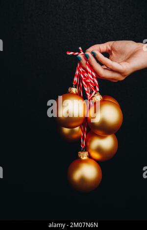 goldene weihnachtsbälle in Frauenhand isoliert auf schwarzem Hintergrund. Neujahrskarte, Werbung, Foto für Geschichte, Glückwunsch Stockfoto