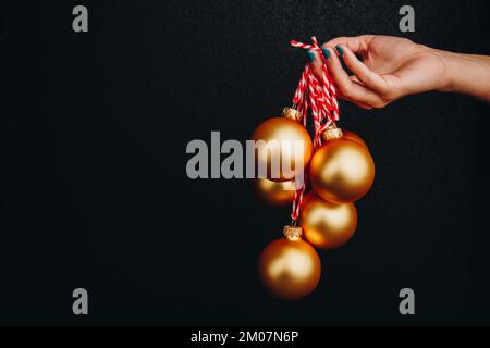 goldene weihnachtsbälle in Frauenhand isoliert auf schwarzem Hintergrund. Neujahrskarte, Werbung, Foto für Geschichte, Glückwunsch Stockfoto