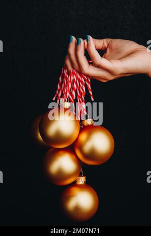 goldene weihnachtsbälle in Frauenhand isoliert auf schwarzem Hintergrund. Neujahrskarte, Werbung, Foto für Geschichte, Glückwunsch Stockfoto