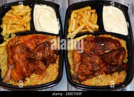 Arabische syrische Küche mit maschinengegrilltem Hähnchen mit farbenfrohem Basmati-Reis und Pommes Frites, Fingerkartoffeln serviert in einem schwarzen Einweg-Pl Stockfoto