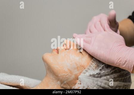 Konzept Kosmetikerin. Die Hände eines Kosmetikers haben einer Frau Creme ins Gesicht gesteckt. Kosmetikerin trägt eine Creme auf das Gesicht des Mädchens auf Stockfoto