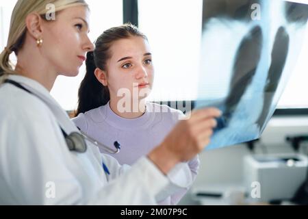 Junge Ärztin, die dem Patienten ein Röntgenbild der Lunge zeigt. Stockfoto