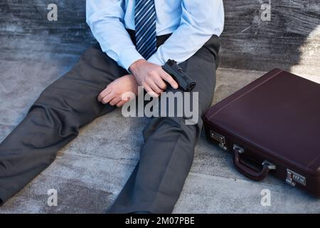 Selbstmord begehen. Ein Geschäftsmann, der mit einer Waffe neben ihm sitzt. Stockfoto