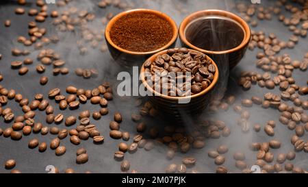 Tassen Kaffee unter ausgewählten und kalibrierten Arabica-Kaffeebohnen, verteilt auf schwarzem Hintergrund, drei aromatische Tassen Kaffee in einem Paar. Stockfoto