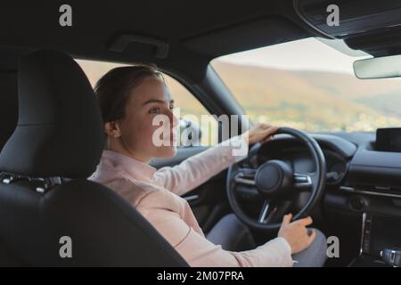 Aufgeregte junge Frau, die ihr Elektroauto fährt. Stockfoto