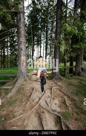 Vorokhta, Ukraine 12. Juni 2022: Ein Junge schwingt auf einer Schaukel im Wald, Sommerurlaub im Wald, Karpaten-Wälder. Stockfoto