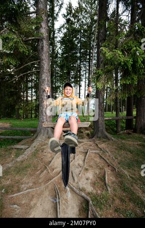 Vorokhta, Ukraine 12. Juni 2022: Ein Junge schwingt auf einer Schaukel im Wald, Sommerurlaub im Wald, Karpaten-Wälder. Stockfoto