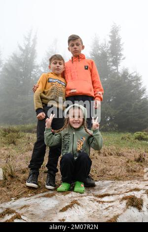 Vorokhta, Ukraine am 12. Juni 2022: Touristen in leuchtenden Kleidern ruhen sich in den Karpaten aus, drei Kinder in der Nähe der Schneereste in den Bergen. Stockfoto