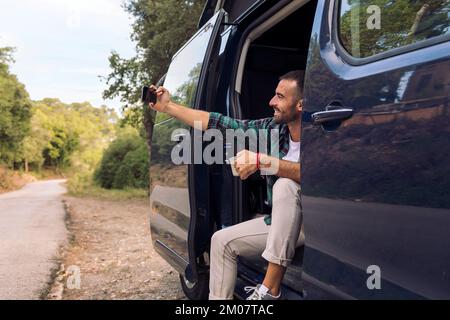 Ein Mann, der ein Selfie macht, sitzt in der Tür seines Lieferwagens Stockfoto