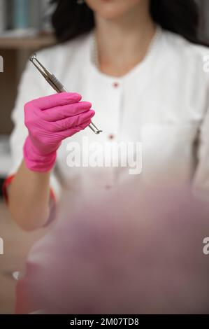 UNO Löffel in den Händen einer Kosmetikerin, Kosmetikerin Werkzeuge zur Gesichtsreinigung, Kosmetikerin in rosa Handschuhen. Stockfoto