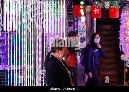 Hongkong, Hongkong, China. 5.. Dezember 2022. Menschen mit Gesichtsmaske gehen vorbei an einem Lichterdekorationsladen im Bezirk Kowloon, wo die SAR-Flagge von Hongkong und Chinas Nationalflagge ausgestellt sind, inmitten zivilen Ungehorsams auf dem chinesischen Festland über ''Zero-Covid'' Maßnahmen. Die Nachfrage der Wirtschaft in Hongkong nach einer Lockerung der Covid-Beschränkungen bei der Einreise in die Stadt steigt, während die "Zero-Covid"-Politik Pekings landesweite Empörungen und Proteste im Weißbuch in China ausgelöst hat. (Kreditbild: © Daniel Ceng Shou-Yi/ZUMA Press Wire) Stockfoto