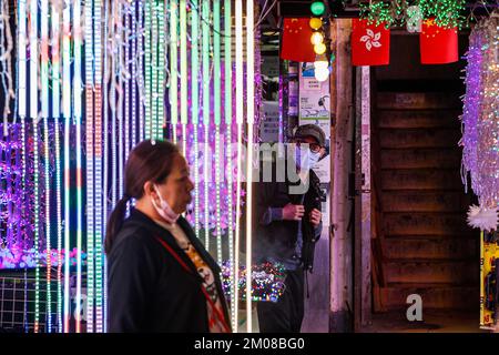 Hongkong, Hongkong, China. 5.. Dezember 2022. Menschen mit Gesichtsmaske gehen vorbei an einem Lichterdekorationsladen im Bezirk Kowloon, wo die SAR-Flagge von Hongkong und Chinas Nationalflagge ausgestellt sind, inmitten zivilen Ungehorsams auf dem chinesischen Festland über ''Zero-Covid'' Maßnahmen. Die Nachfrage der Wirtschaft in Hongkong nach einer Lockerung der Covid-Beschränkungen bei der Einreise in die Stadt steigt, während die "Zero-Covid"-Politik Pekings landesweite Empörungen und Proteste im Weißbuch in China ausgelöst hat. (Kreditbild: © Daniel Ceng Shou-Yi/ZUMA Press Wire) Stockfoto