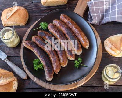 Gebratene Wurst mit Brötchen und Senf. Traditionelle deutsche Mahlzeit auf Holztisch. Flach verlegt Stockfoto