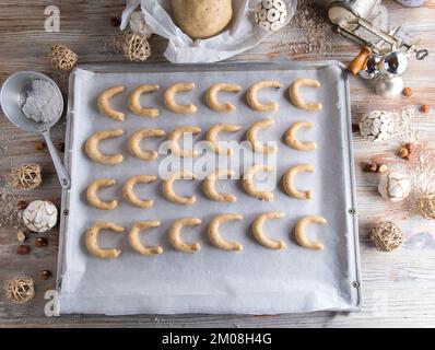 Vanillekipferl oder Vanillesoncent roh und ungebacken auf einem Backblech mit Teig und Küchenutensilien und weihnachtsdekoration. Flach verlegt Stockfoto