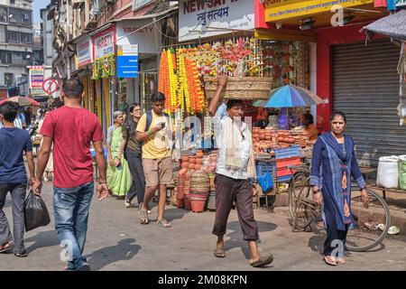 Straßenszene in Bhuleshwar / Kalbadevi Marktbereich in Mumbai, Indien, ein Portier mit einem Korb auf dem Kopf, der vorbeifährt Stockfoto