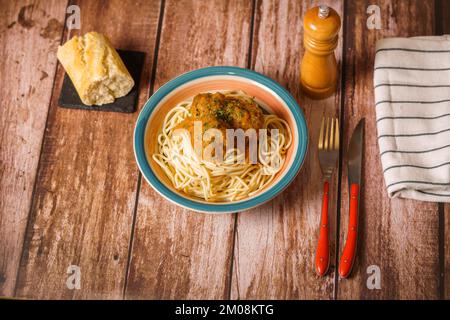 Teller mit Fleischbällchen mit Spaghetti mit Besteck und Brot- und Pfefferstreuer auf einem Holztisch Stockfoto
