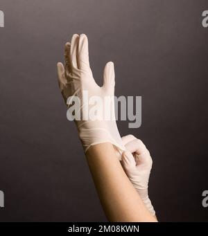 Weibliche Hände, die weiße Latexhandschuhe anziehen Stockfoto