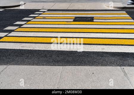 Gestreiftes gelb-weißes Fußgängerzebra auf grauem Asphalt, abstrakter Hintergrund. Fußgängerübergang auf der Straße für die Sicherheit der Menschen. Stockfoto