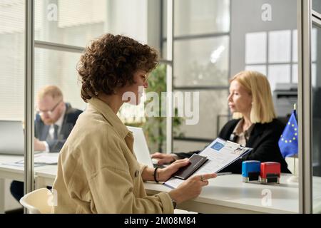 Seitliches Porträt einer lächelnden jungen Frau mit genehmigtem Visumantrag im Einwanderungsamt Stockfoto
