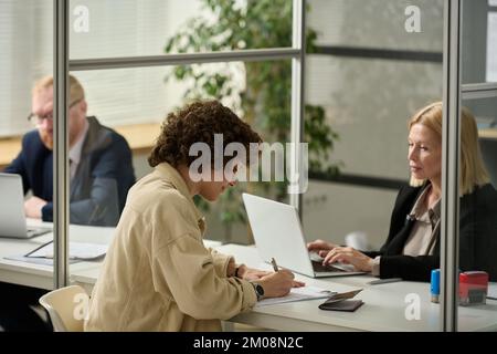 Seitenbild einer jungen Frau beim Ausfüllen des Antragsformulars im Konsulat Stockfoto