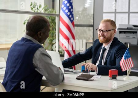 Portrait eines freundlichen, lächelnden Arbeiters, der einen älteren schwarzen Mann im US-Einwanderungsamt berät Stockfoto