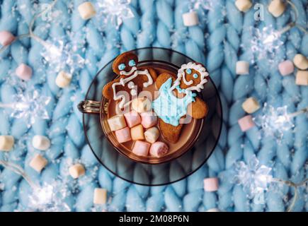 Konzept des Paarheims-Weihnachtsfeiertags. Ein Paar Frau und ein Mann aus Lebkuchen, der in einer Tasse heiße Schokolade mit Marshmallows einweicht, gemütlich. Stockfoto