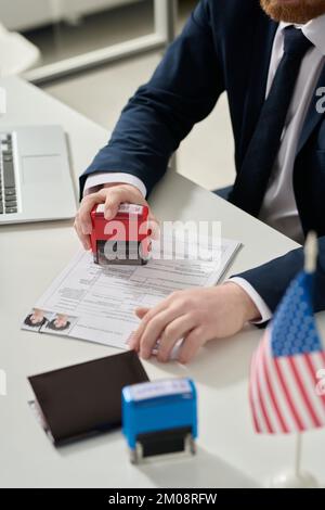 Nahaufnahme eines männlichen Arbeiters, der einen abgelehnten Stempel auf einem Visumantrag in der US-Einwanderungsbehörde angebracht hat Stockfoto