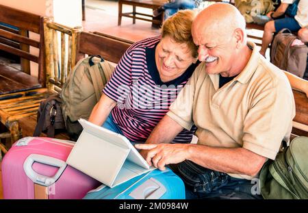 Glückliches Seniorenpaar sitzt mit digitalem Laptop und reist mit Gepäck während einer Abenteuerreise um die Welt - Konzept eines aktiven älteren Lebensstils Stockfoto