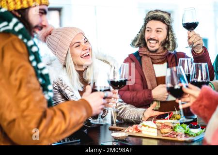 Junge Leute toasten Rotwein auf der Restaurantterrasse - glückliche Freunde, die sich in Winterkleidung in der Weinkellerei-Bar amüsieren Stockfoto