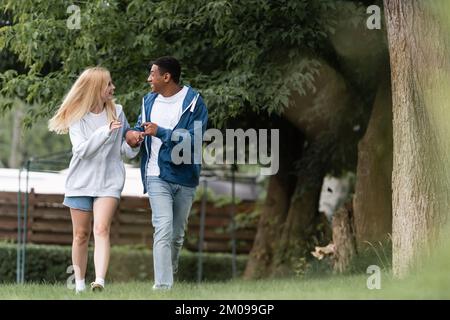 Ein glückliches, multiethnisches Paar, das im Park spaziert und sich unterhält Stockfoto