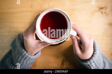Tasse roter Farbtee in weiblichen Händen, Draufsicht. Stockfoto