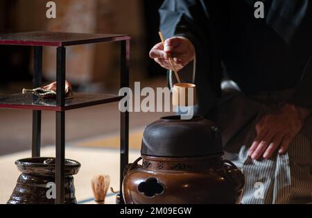 Japanischer Mann in traditionellem Kimono, während der Teezeremonie. Schwarzer Hintergrund.. Stockfoto