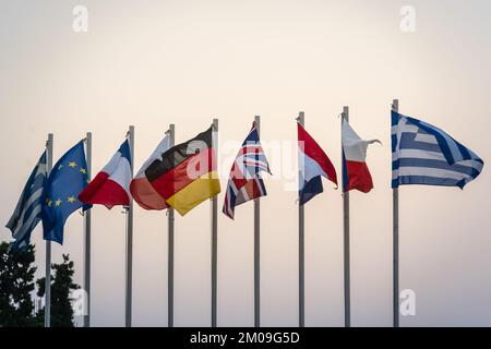 Eine Reihe von Flaggen einiger Länder der Europäischen Union, die auf Metallmasten gegen bewölkten Dämmerhimmel winken Stockfoto