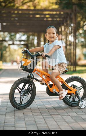 Glückliches kleines Mädchen, das Fahrrad fährt und aufgeregt aussieht Stockfoto