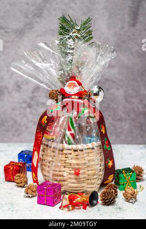 Neujahrsgeschenk. Weihnachtsgeschenk mit Korb auf grauem Hintergrund. Paket mit Schokolade, Nüssen, Snacks Stockfoto