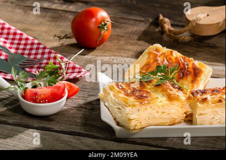 Wassergebäck auf dem Teller. Zusammensetzung von Wassergebäck, Tomaten, heißem Pfeffer und Oliven auf altem Holztisch. Stockfoto