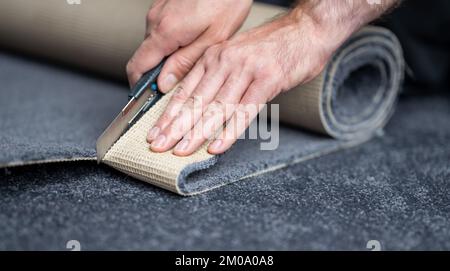 Handwerker, der einen neuen Teppich mit einem Teppichschneider schneidet. Stockfoto