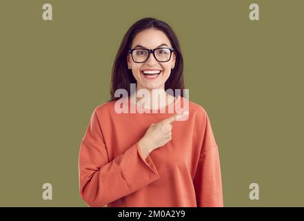 Eine Frau mit einem komischen, geschossenen Gesicht, die mit dem Finger zur Seite zeigt und ein Angebot oder einen Werbevertrag zeigt. Stockfoto