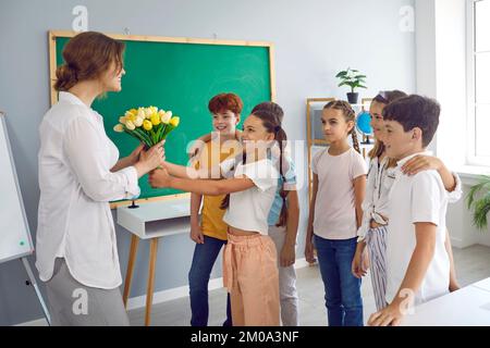 Glückliche Kinder, Jungen und Mädchen, die Blumen an Grundschullehrer übergeben, stehen im Klassenzimmer Stockfoto