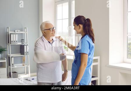 Der ältere Mann mit dem verletzten Arm diskutiert die Behandlung mit einer freundlichen Therapeutin. Stockfoto